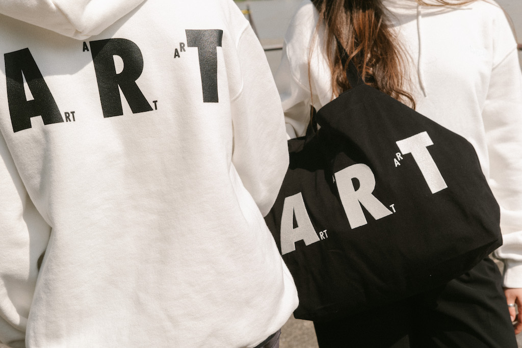 A white hoodie and a black tote bag printed with the word "ART".