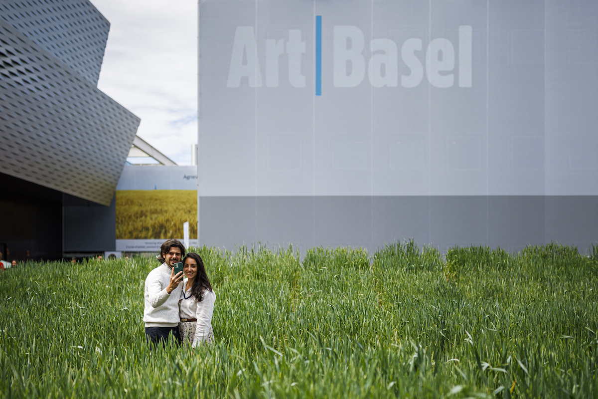 Visitors take a selfie in front of the installation "Honouring, Wheatfield - A Confrontation", 2024, by American artist Agnes Denes at the Messeplatz Project at Art Basel fair for Modern and contemporary art, in Basel, northern Switzerland, on June 11, 2024. (Photo by Valentin FLAURAUD / AFP) / RESTRICTED TO EDITORIAL USE - MANDATORY MENTION OF THE ARTIST UPON PUBLICATION - TO ILLUSTRATE THE EVENT AS SPECIFIED IN THE CAPTION