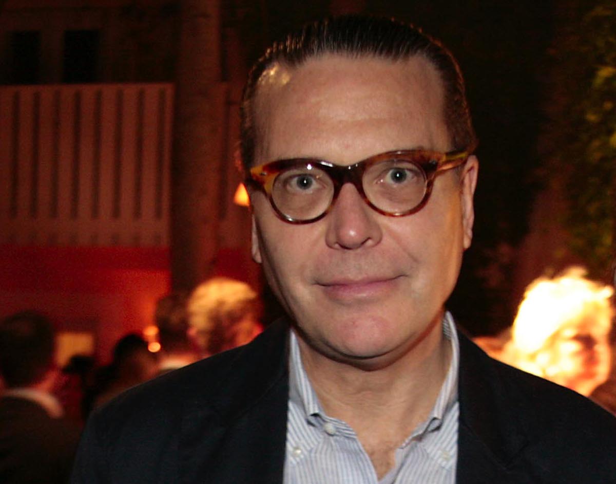 A white man in horn-rimmed glasses and a suit jacket at party.