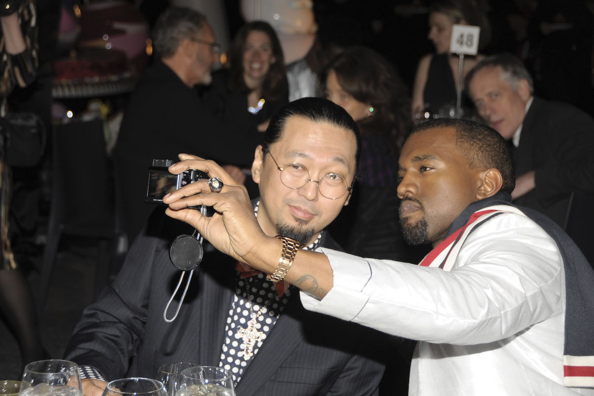 A Black man holding up a camera to take a selfie with an Asian man at a party.