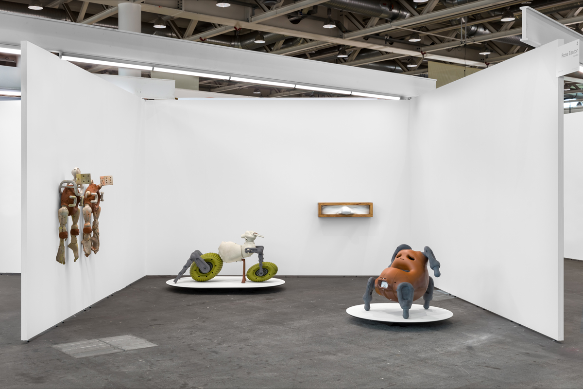 View of an art fair booth showing four sculptures, two in the center and two on the walls.