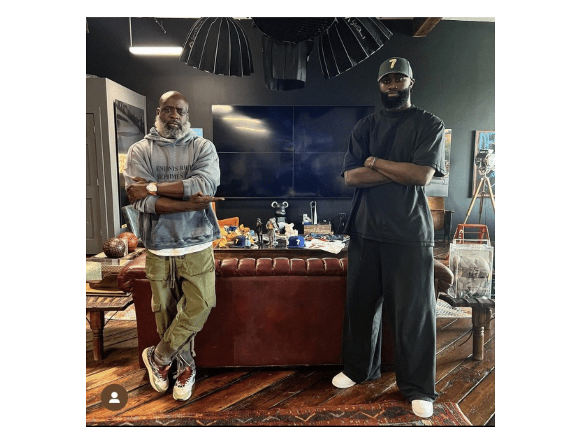 Two men stand next to a brown leather sofa.