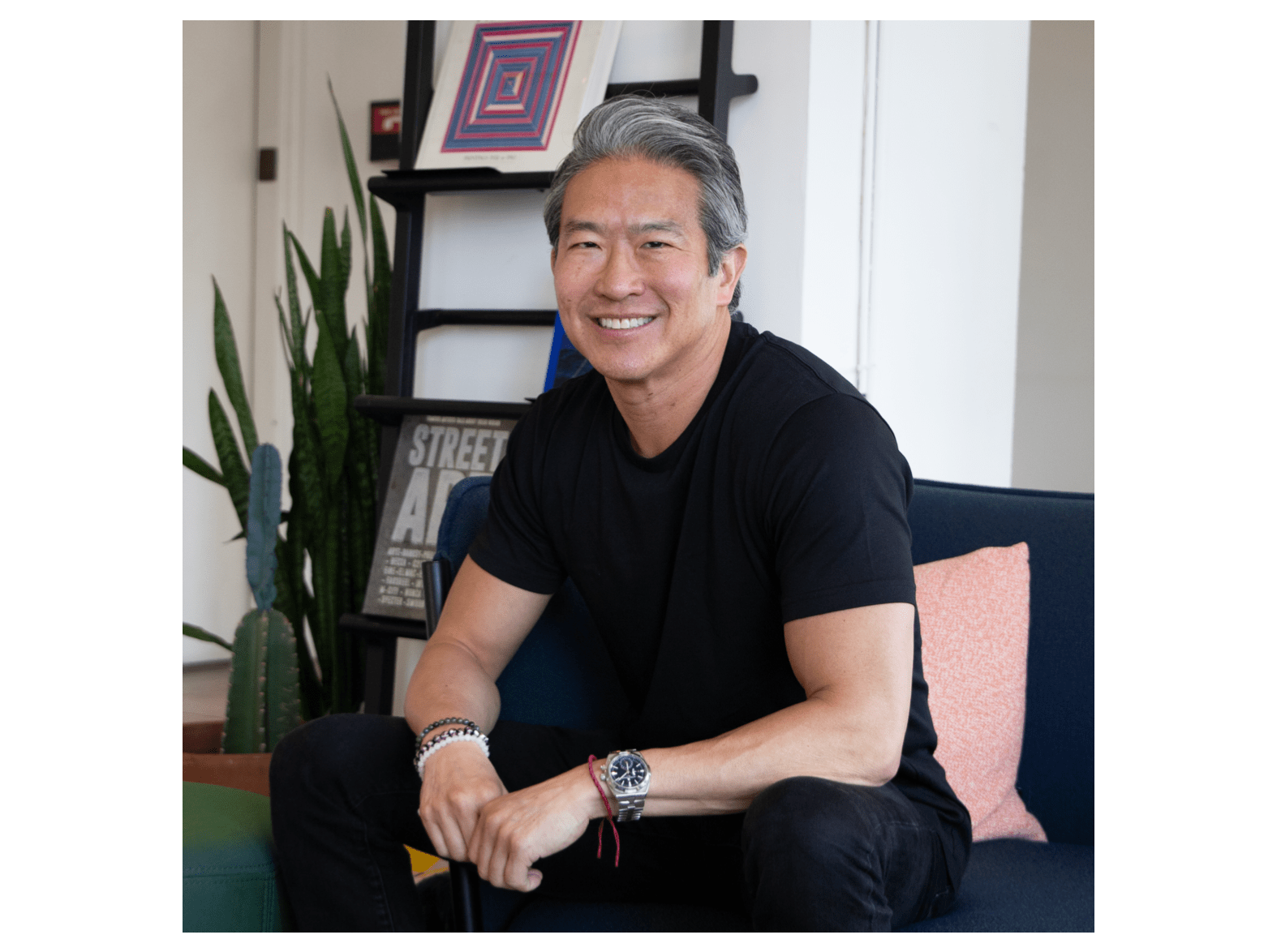 A man in black with a shock of silvery salt and pepper hair smiles at the viewer.